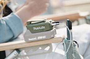 woman sitting in chain while Makita Outdoor Adventure portable battery charges her phone