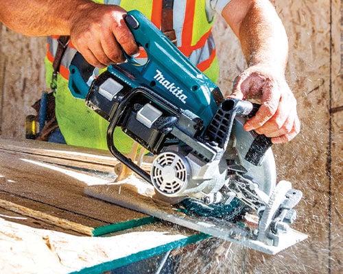 A man using an 18V Makita rear handle circular saw to cut a piece of wood.