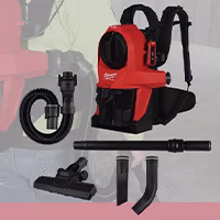 A close-up cropped image focusing on a red and black Milwaukee backpack vacuum and its accessories layout. Below the vacuum unit, the included attachments are clearly displayed: a flexible black hose, a straight extension wand, a wide floor tool, a slim crevice tool, and a curved nozzle piece. A faded image of a worker wearing the vacuum is visible in the background.